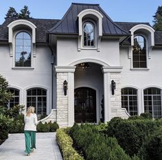 a woman walking in front of a large white house with arched windows and black roof