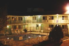 an apartment building at night with pool in the foreground and chairs on the other side