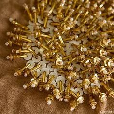 many gold colored screws are laying on a brown surface with white dots and flowers