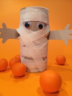 a toilet paper roll with eyes and arms wrapped around oranges on an orange background