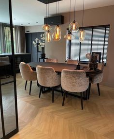 a dining room table with chairs and lights hanging from it's ceiling, in front of a large window