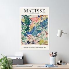 a poster on the wall above a desk with a plant and other office supplies in front of it