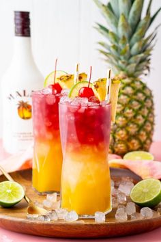 two glasses filled with drinks sitting on top of a wooden tray next to a pineapple