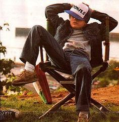 a young man sitting in a chair with his hat over his head and hands behind his head