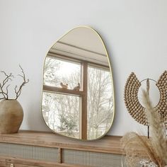 a mirror sitting on top of a wooden dresser next to a vase with dried flowers