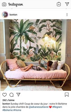 a person laying on a bed in front of a wall with plants and birds painted on it