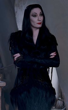 a woman with long black hair wearing a fur coat and holding her arms crossed in front of her chest