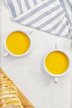 two bowls of soup next to a loaf of bread on a white tablecloth and towel