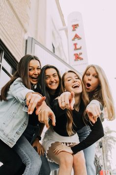 four young women pointing their fingers at the camera while standing in front of a building