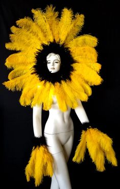 a white mannequin with yellow feathers on it's head and arms, standing in front of a black background