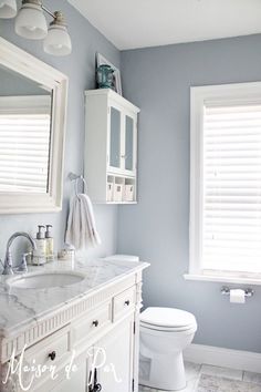 a bathroom with blue walls and white fixtures, including a sink, toilet, and window