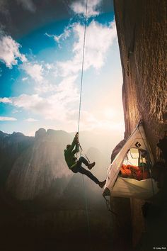 a man hanging from the side of a cliff while holding onto a rope with his hands