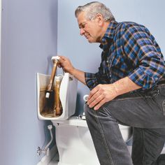 a man sitting on top of a toilet holding a plunger and bottle in it