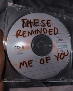 a cd with writing on it is being held up by someone's hand in the background