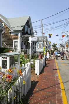 people are walking down the sidewalk in front of some houses and shops on a sunny day