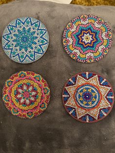 four circular beaded coasters sitting on top of a gray cushion, each decorated with different colors and designs