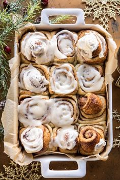 cinnamon rolls with icing in a baking dish on a table surrounded by christmas decorations