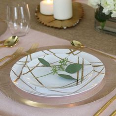 a white plate topped with green leaves on top of a table next to gold utensils