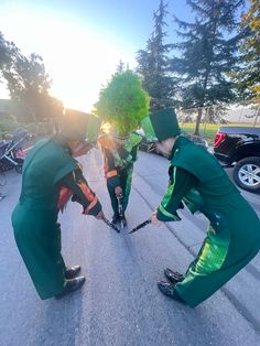 three people dressed in green are playing with each other on the street while one person is wearing a wig