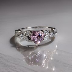 a pink heart shaped diamond ring on a white surface