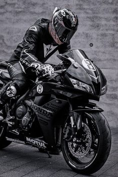 a man riding on the back of a motorcycle next to a cement wall and wearing a helmet