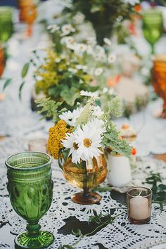 a table topped with lots of vases filled with white and yellow flowers next to candles