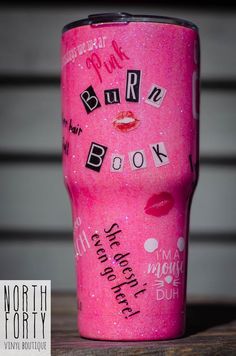 a pink tumbler with writing on the side and lips painted on it, sitting on top of a wooden table