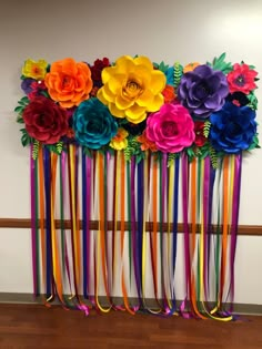 colorful paper flowers and ribbons are hanging on the wall in front of a wooden floor