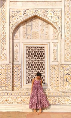 a woman standing in front of a white wall with intricate carvings on the doors and windows