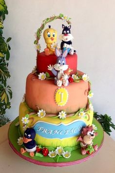 a three tiered cake with cartoon characters on it's sides and flowers around the edges