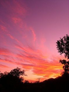 the sky is pink and purple as the sun sets in the distance behind some trees