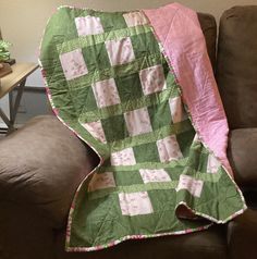 a green and pink blanket sitting on top of a brown couch