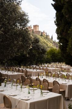 an outdoor dining area with tables and chairs covered in white tablecloths surrounded by trees