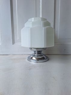 a white glass candle holder sitting on top of a wooden table next to a door