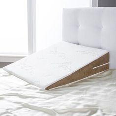 a bed with a pillow on top of it next to a white headboard and window