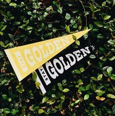 a yellow and white pennant with the word golden on it in front of some green leaves