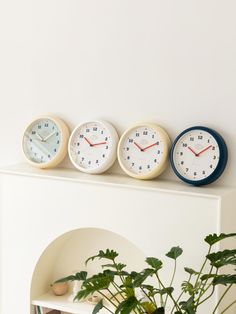 three clocks are sitting on top of a shelf next to a potted plant in a living room