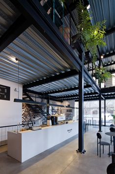 the interior of a restaurant with tables, chairs and plants hanging from the metal roof