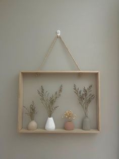 three vases are on a shelf with rope hanging from the wall above them, and one is filled with flowers