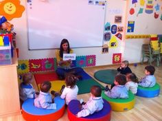 a woman reading to children in a classroom with colorful bean bag chairs and rugs on the floor