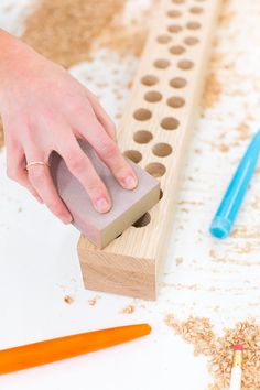 a person is using a rubber stamp on a piece of wood with pencils and crayons in the background