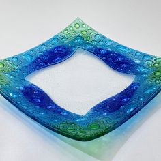 a blue and green square shaped glass plate on a white table top with water droplets