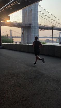 a man running under a bridge with the sun setting in the back ground and water behind him