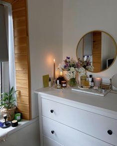 a white dresser with candles and flowers on it in front of a window sill