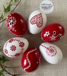 four red and white painted eggs sitting on top of a table next to a plant