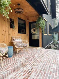 two wicker chairs sitting on top of a brick patio next to a black door