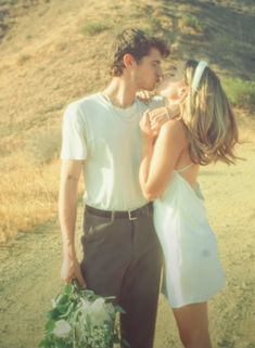 a man and woman standing next to each other in front of a hill with flowers