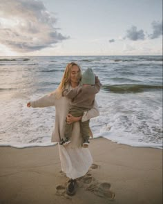 a woman holding a child on top of her back while standing in front of the ocean