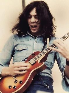 a man with long hair playing an electric guitar