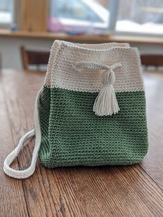 a green and white crochet bag sitting on top of a wooden table next to a window